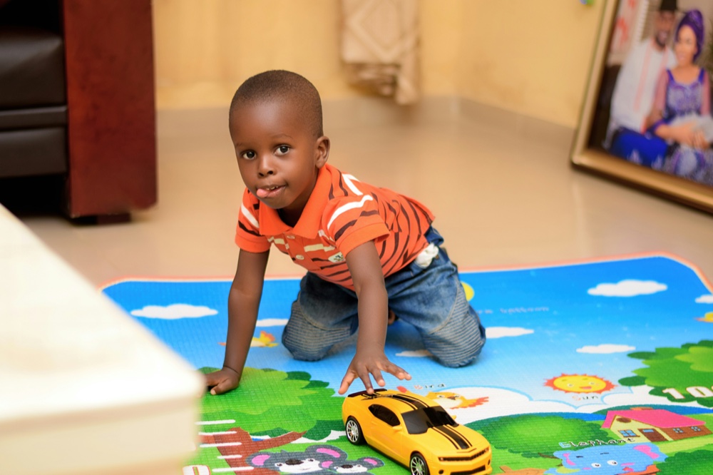A toddler kneeling on a brightly patterned play mat, pushing a toy car
