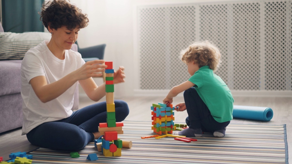 An adult and a child stacking wooden blocks into towers on a rug