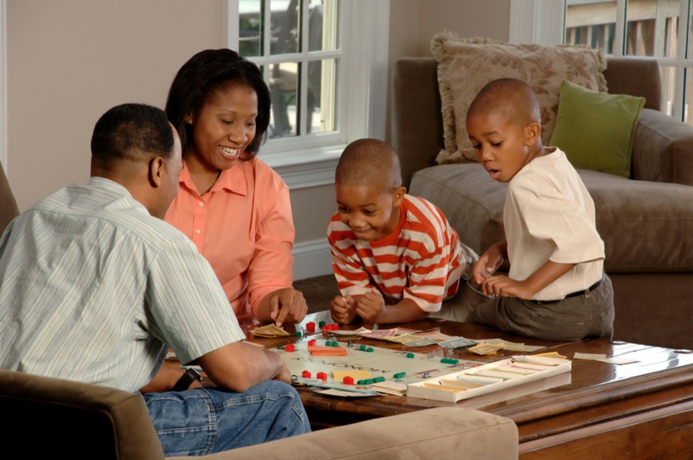 Two adults and two young children playing a board game together in a living room