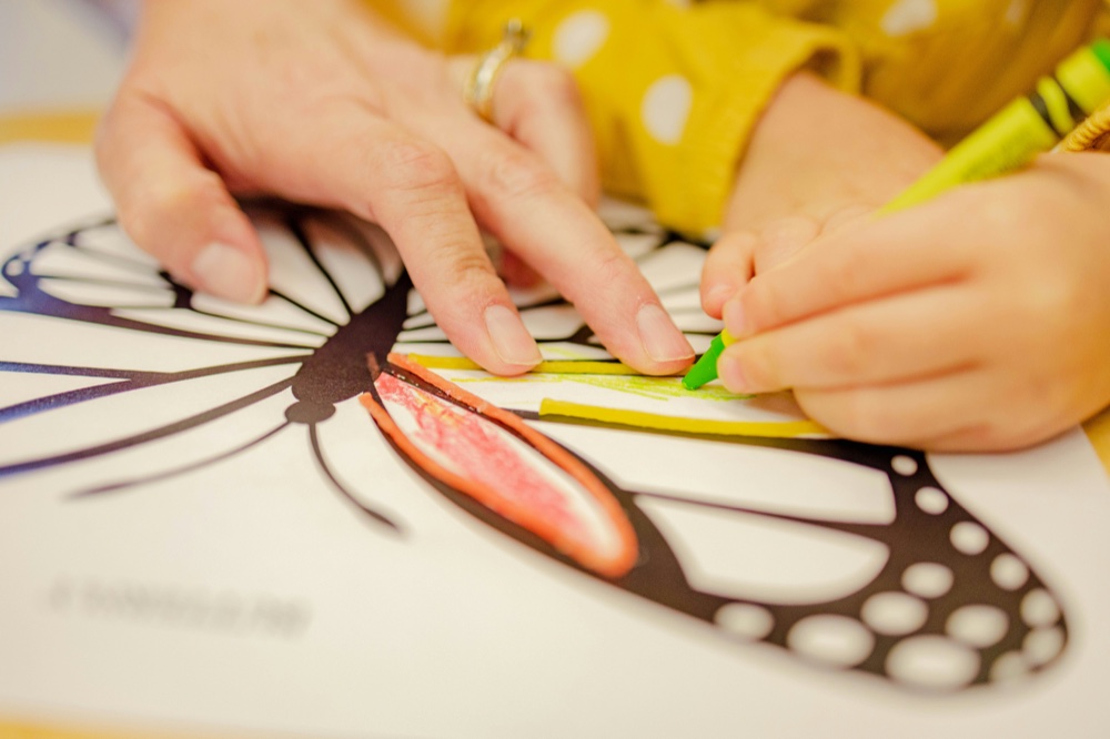 An adult steadying a large butterfly drawing while a child colours it with a felt pen