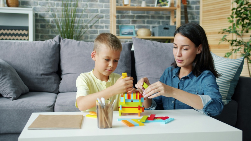 An adult and a child building a tower from coloured blocks at a table