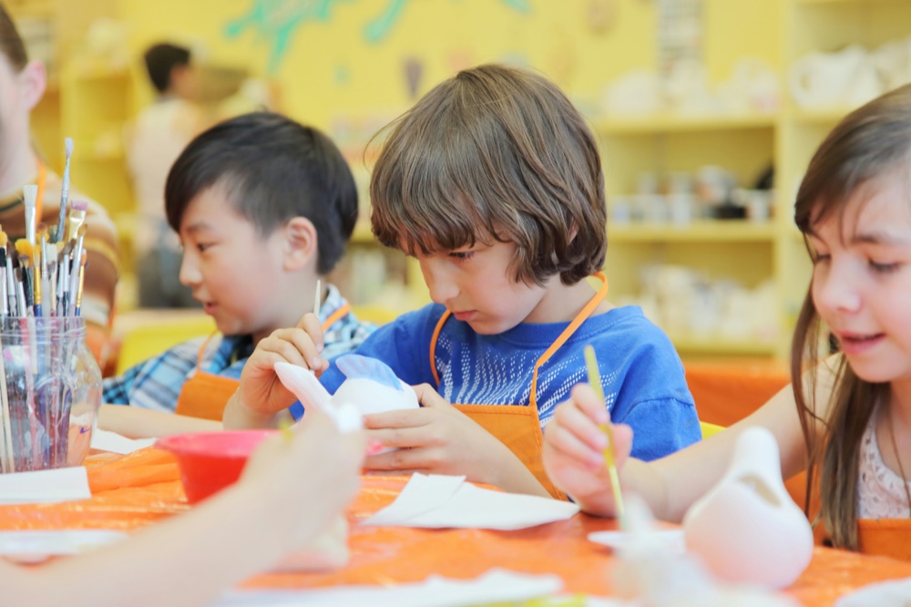 Several children working on craft projects around a table in a bright studio
