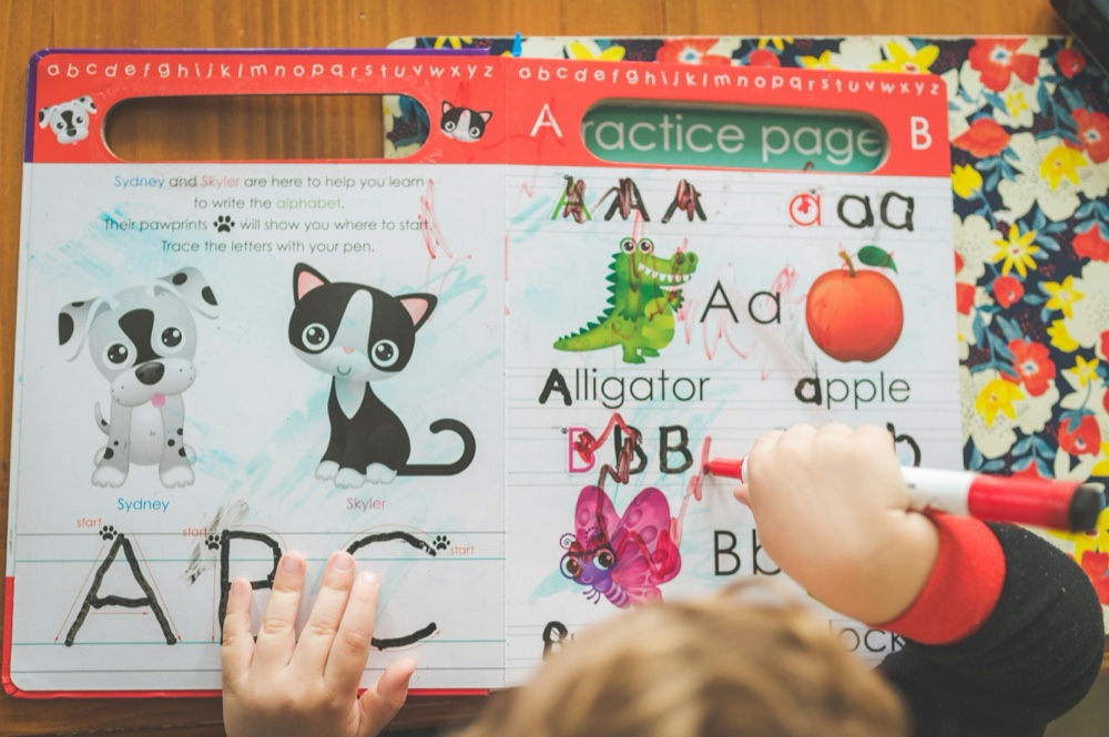 A child tracing letters on an illustrated alphabet practice page