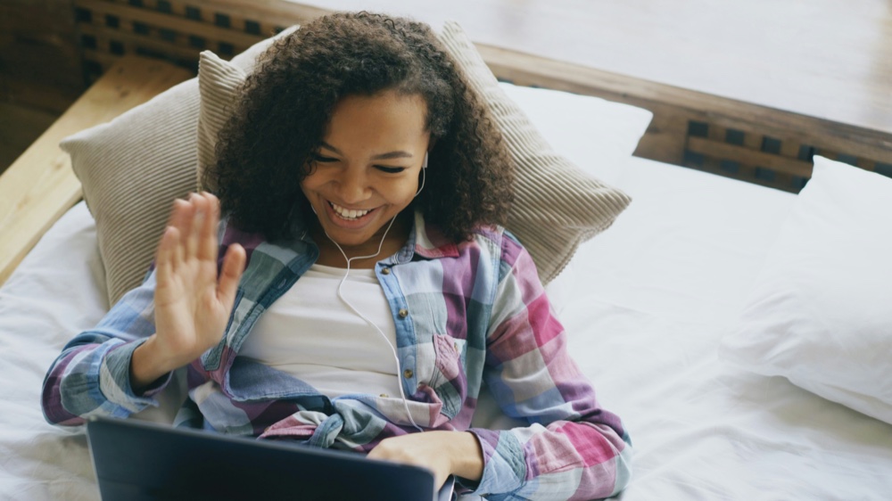 A person waving at a laptop screen during a video call
